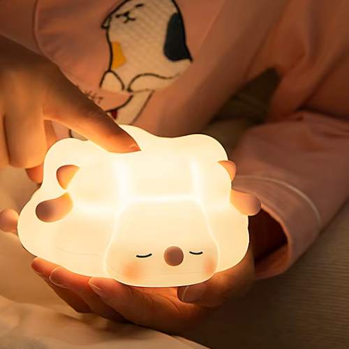 petite fille qui tient la veilleuse bebe mouton rose dans ses mains, dans son lit