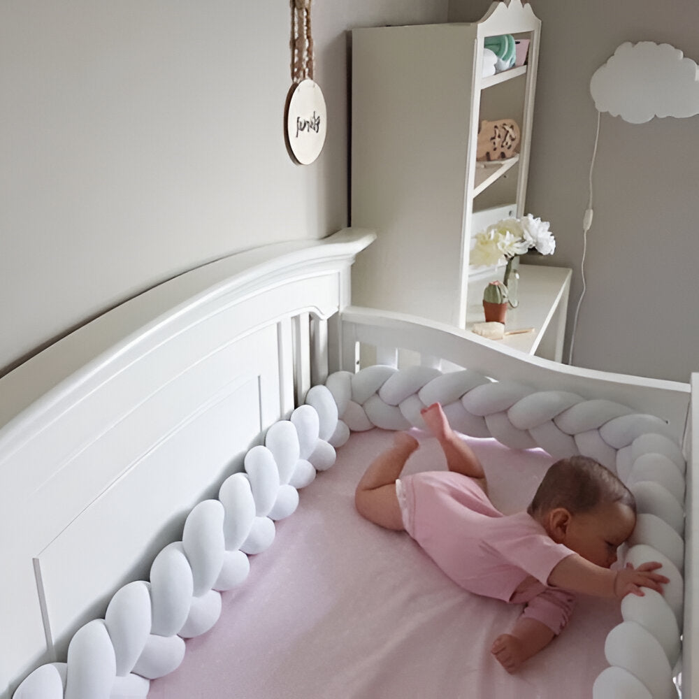 bébé qui joue dans son lit avec sa tresse de lit blanche